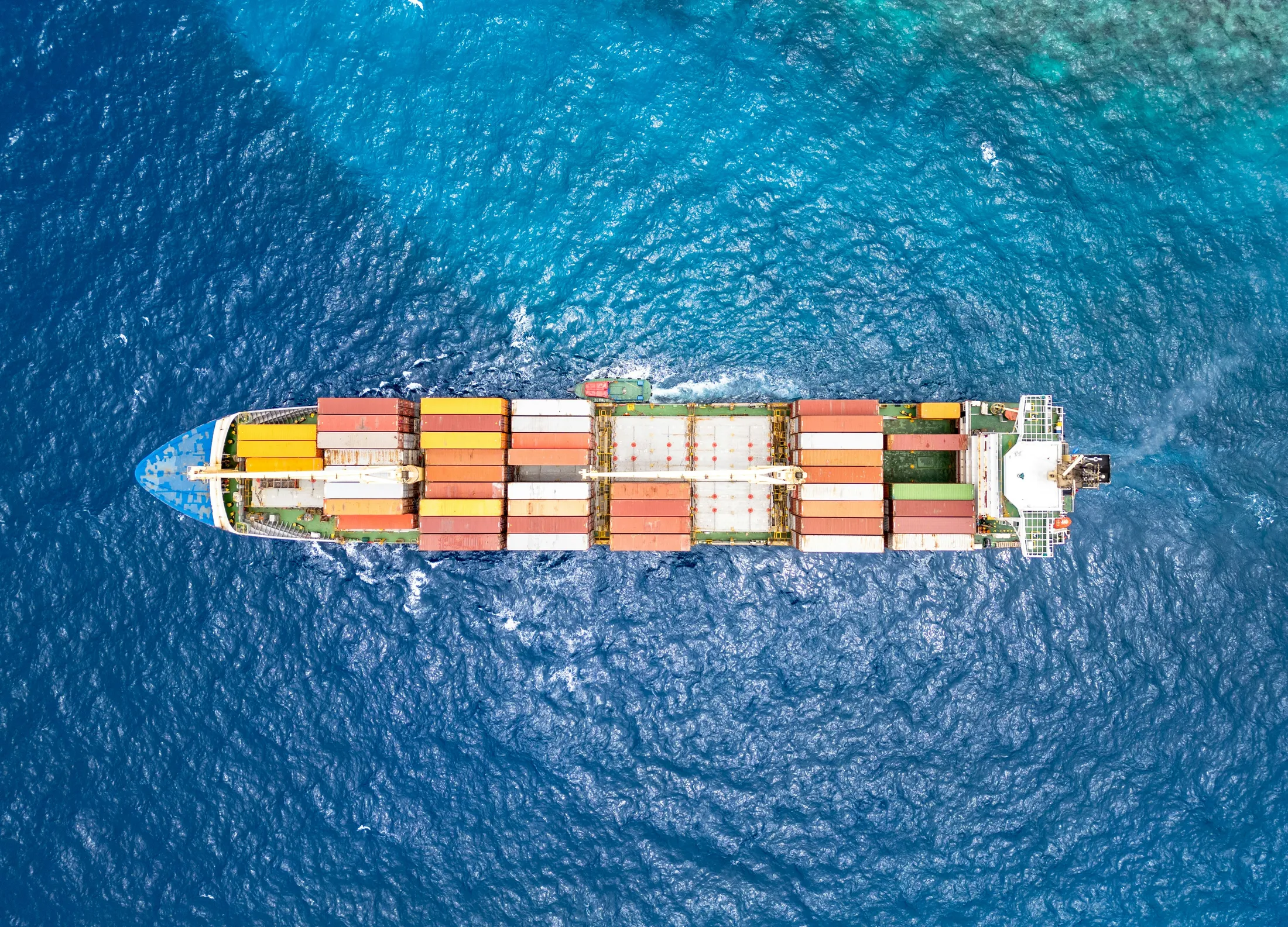 Aerial view of a container ship on turquoise water near a reef