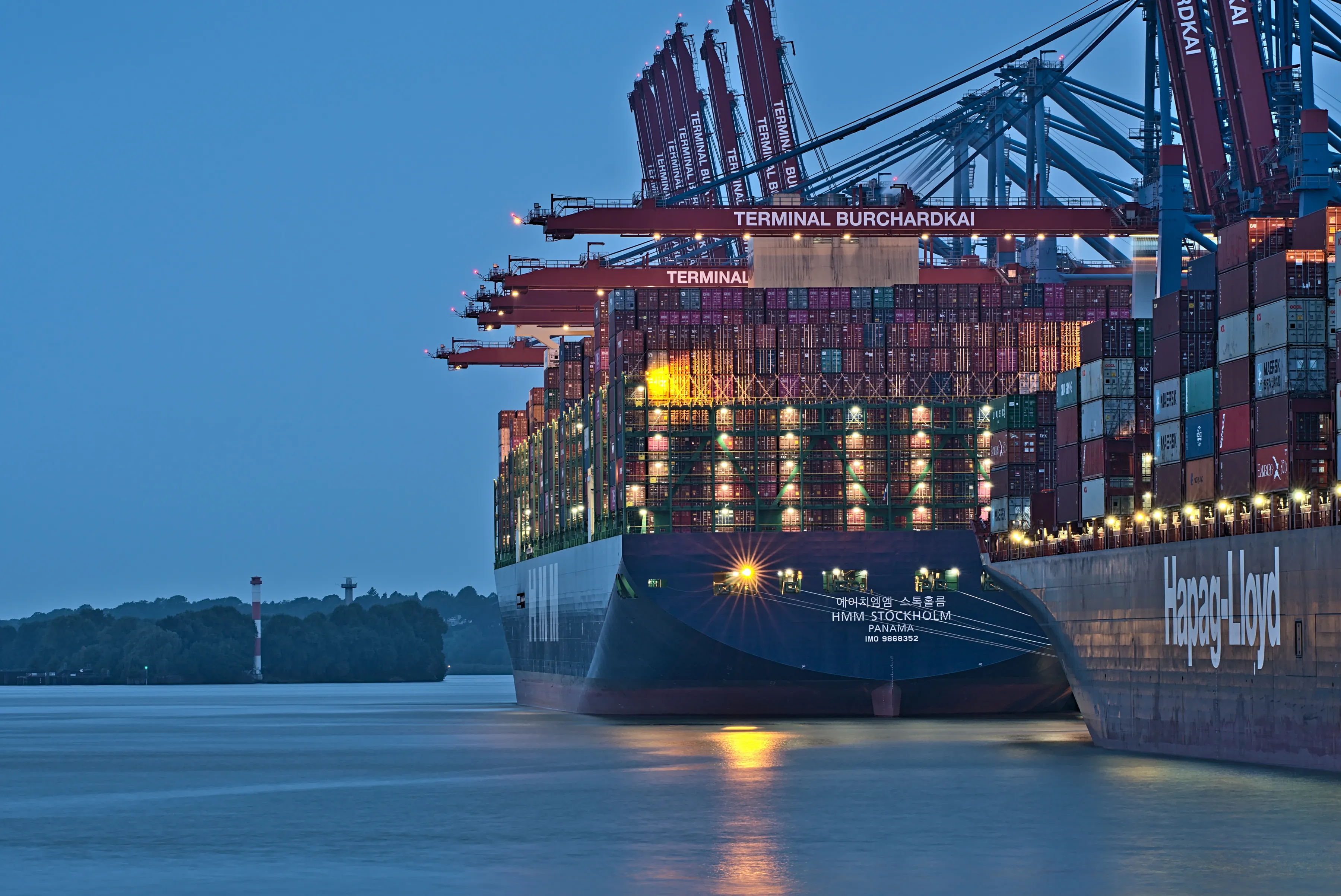 Container terminal at dusk with ships docked beneath gantry cranes