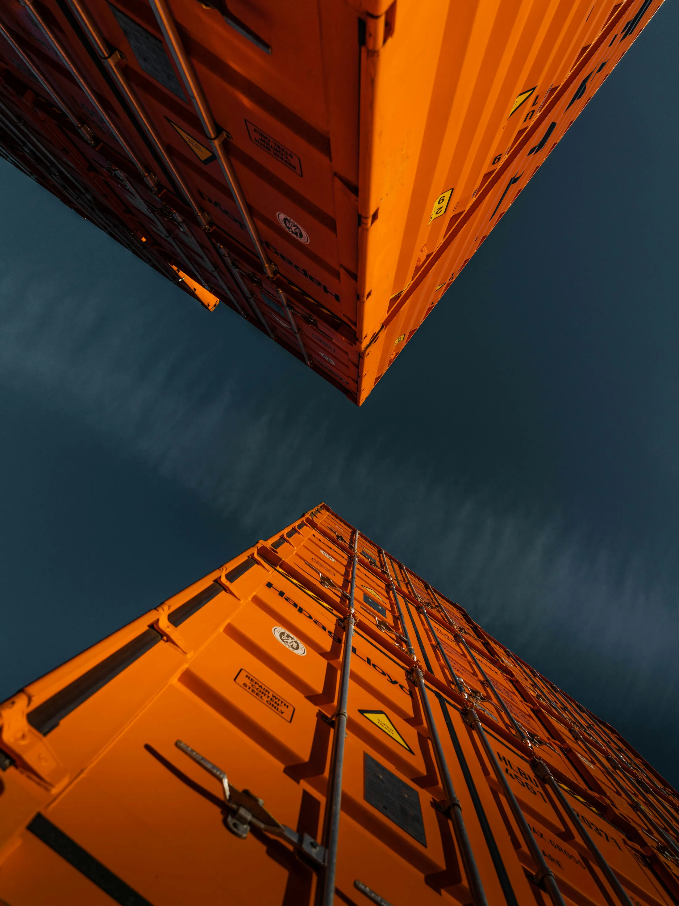 Low-angle symmetrical view of orange shipping containers against the sky