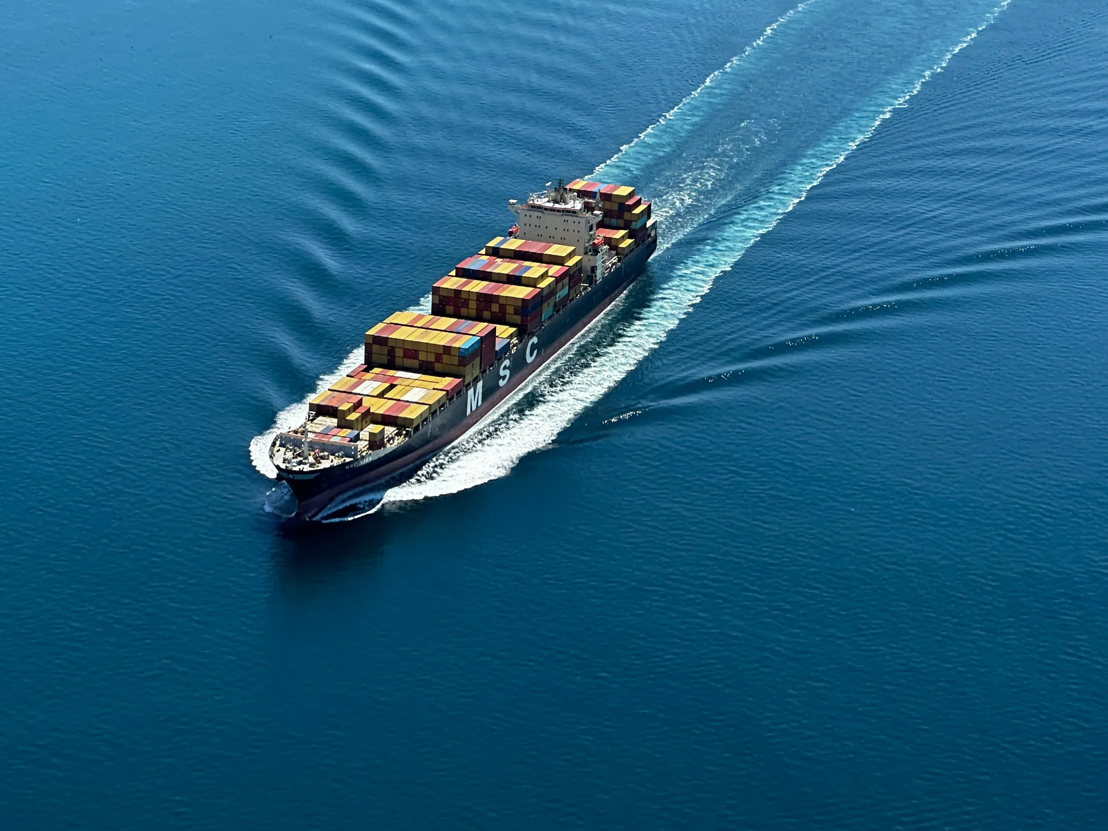 Aerial view of a container ship cutting a diagonal wake across the ocean