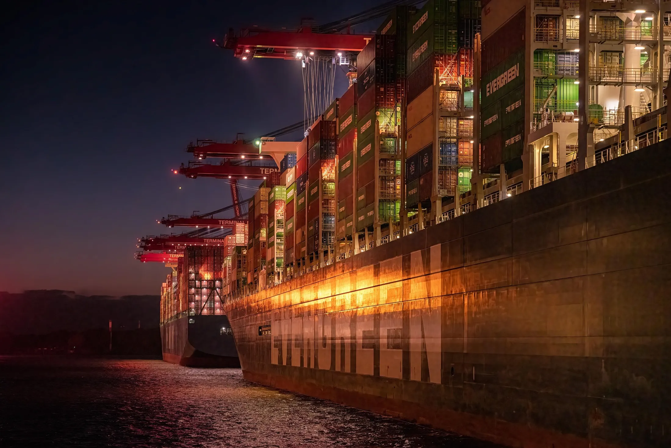 Container ship docked at a terminal at night under gantry cranes